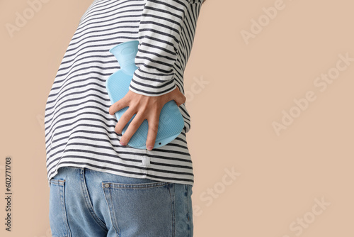 Photography Young man warming his lower back with hot water bottle on beige background, clos