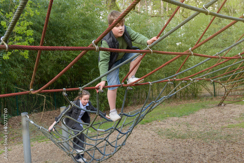 Teenage boy and girl climbing on spider web with expression in public park. Spring sunny day
