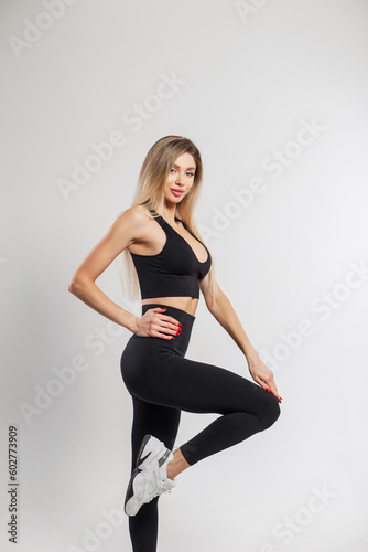 Beautiful athletic young fitness woman model with blond hairstyle in trendy fashion black sportswear outfit with top, leggings and sneakers on a white background in the studio