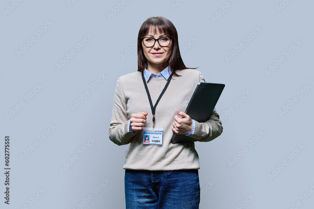 Middle aged woman with educational center badge, laptop on grey background