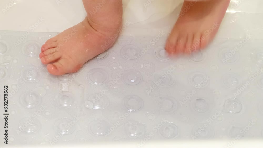 Baby legs is standing on a non-slip mat in the bathtub. Child boy foots washes on the anti slip carpet in the bathroom. Kid about two years old (one year ten months). Baby legs is standing on a non-slip mat in the bathtub. Child boy foots washes on the anti slip carpet in the bathroom. Kid about two years old (one year ten months).