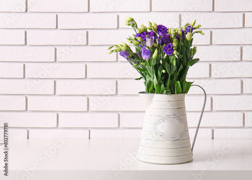 Jug with eustoma flowers on table near white brick wall © Pixel-Shot