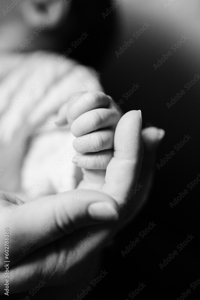 A black and white close-up of a baby's fingers wrapped around her mother's hands. A black and white close-up of a baby's fingers wrapped around her mother's hands.
