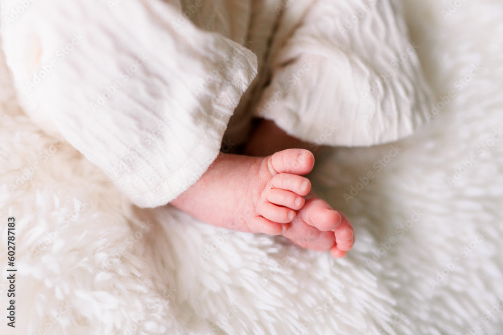 Adorable baby feet close-up. Baby is wearing white pants and lying on a white blanket. Adorable baby feet close-up. Baby is wearing white pants and lying on a white blanket.