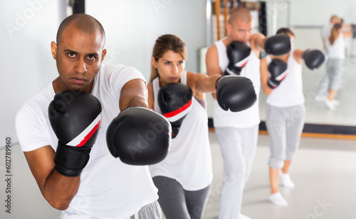 Portrait of confident hispanic male wearing boxing gloves in group workout time in self-defense in gym