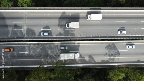 Visão aérea de um carro atravessando a rodovia Mogi Dutra em São Paulo com a sombra das árvores projetando na rodovia. 