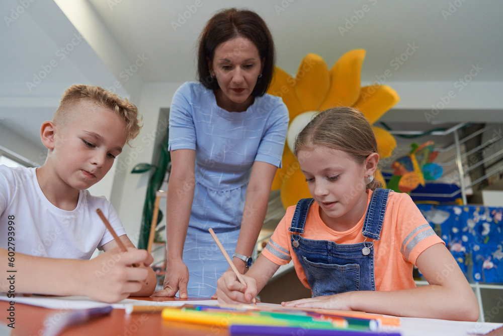 Creative kids during an art class in a daycare center or elementary school classroom drawing with female teacher. Creative kids during an art class in a daycare center or elementary school classroom drawing with female teacher.