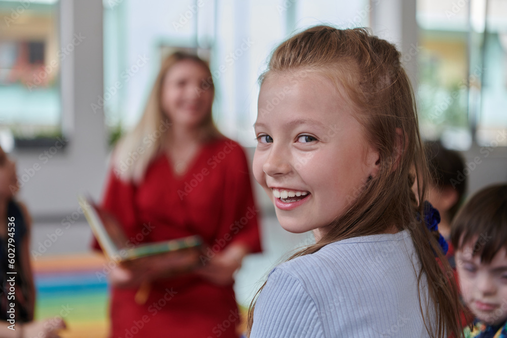 Obraz premium Reading time in an elementary school or kindergarten, a teacher reading a book to children in an elementary school or kindergarten. The concept of pre-school education. Selective focus