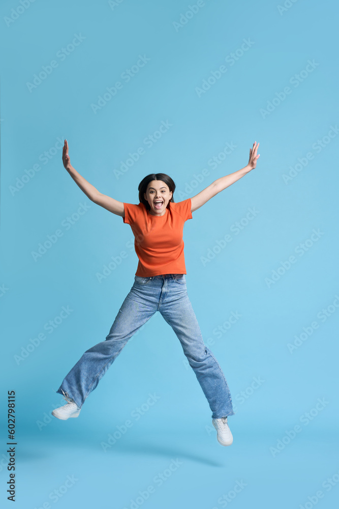 Full size portrait of a beautiful teenager girl smiles at camera and jumps over blue background Full size portrait of a beautiful teenager girl smiles at camera and jumps over blue background