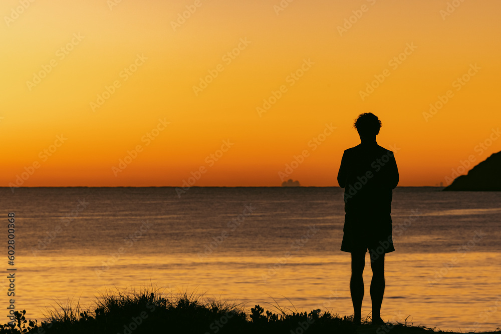 Silhouette of man standing on sand dune overlooking Jimmy's Beach at sunrise. Hawks Nest, NSW Australia