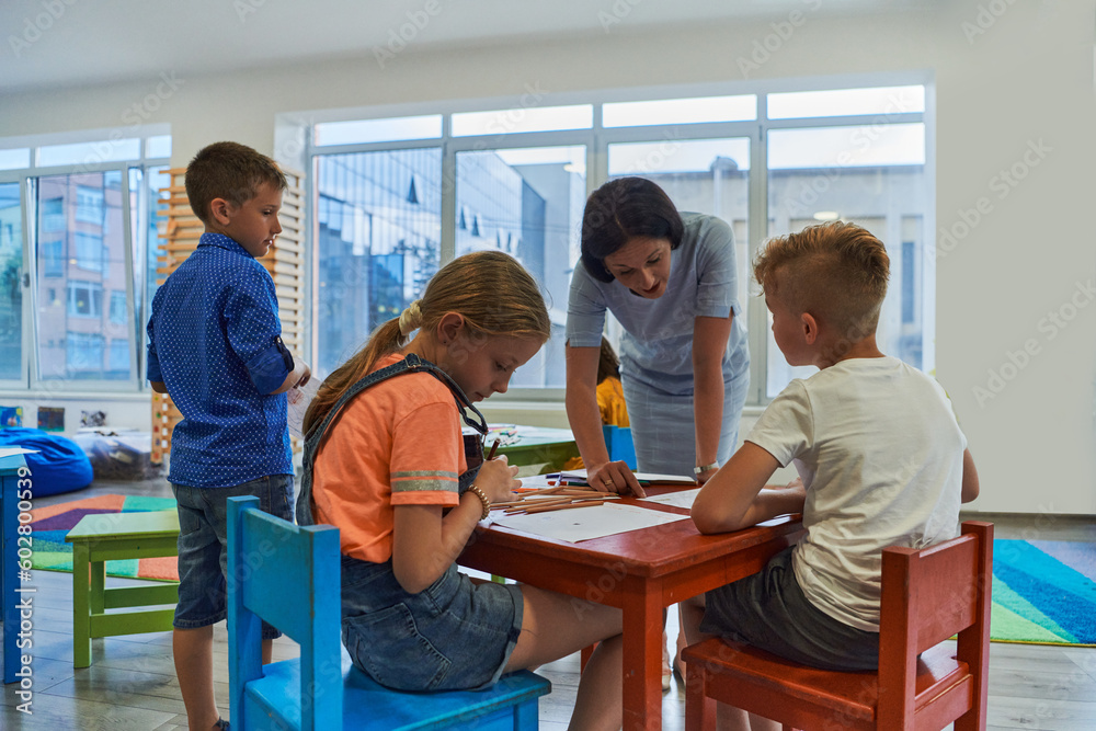 Fototapeta premium Creative kids during an art class in a daycare center or elementary school classroom drawing with female teacher.