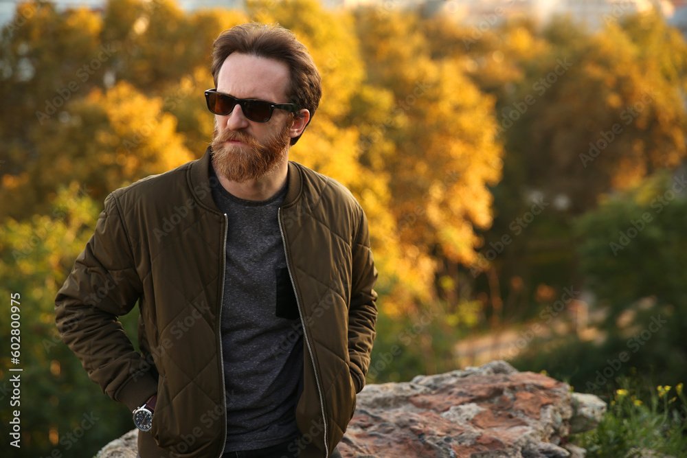 Bearded Caucasian man with sunglasses posing in front of a blurry background with soft natural light. Copy space for text, advertising, message Bearded Caucasian man with sunglasses posing in front of a blurry background with soft natural light. Copy space for text, advertising, message