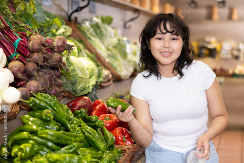 Portrait of positive satisfied girl buying fresh bell peppers in grocery shop