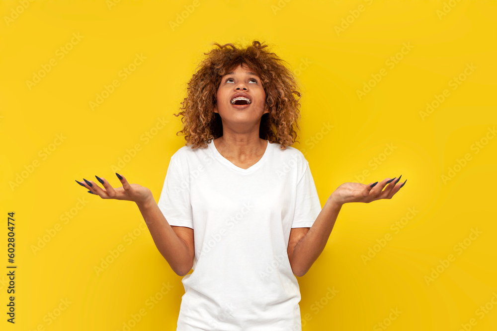 young curly american girl catches spreading her arms to the side and looks up on yellow isolated background young curly american girl catches spreading her arms to the side and looks up on yellow isolated background