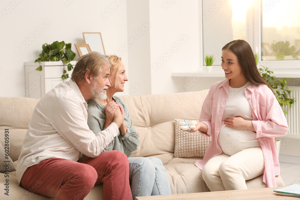 Happy woman showing her parents baby's socks at home. Grandparents' reaction to future grandson