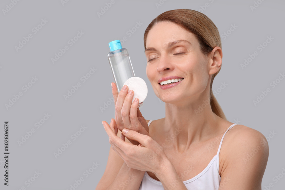 Beautiful woman with makeup remover and cotton pad on gray background, space for text Beautiful woman with makeup remover and cotton pad on gray background, space for text