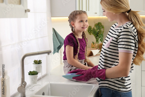 Mother washing plate while speaking with daughter in kitchen