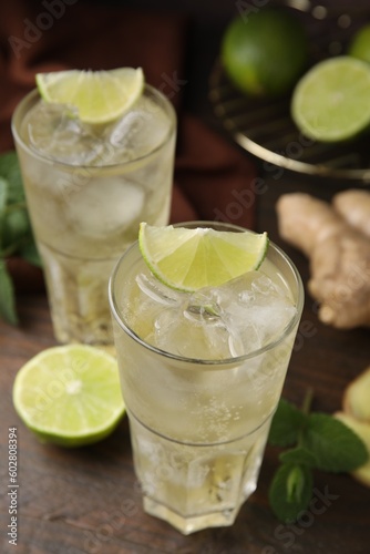 Glasses of tasty ginger ale with ice cubes and ingredients on wooden table, closeup