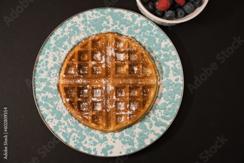 Belgian Waffle on a Teal Plate and Bowl of Berries on a Simple Black Background
