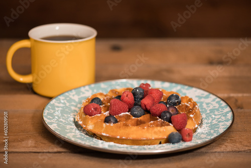 Waffle with powdered sugar, berries, and coffee on a rustic wooden table