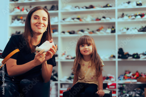 Mother and Daughter Buying Shoes from Footwear Store. Mom helping her little girl finding well-fitting sneakers 