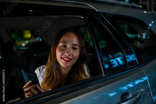 Asian businesswoman commuting from office in Taxi backseat with mobile phone on road in city at night after late work, Beautiful woman using smartphone sitting back seat her car in urban