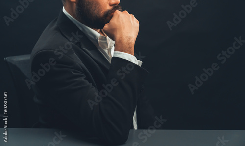 Businessman or lawyer wearing formal black suit sitting at table on isolated black background. Concept of a man with authority and seriousness gesture. equility photo