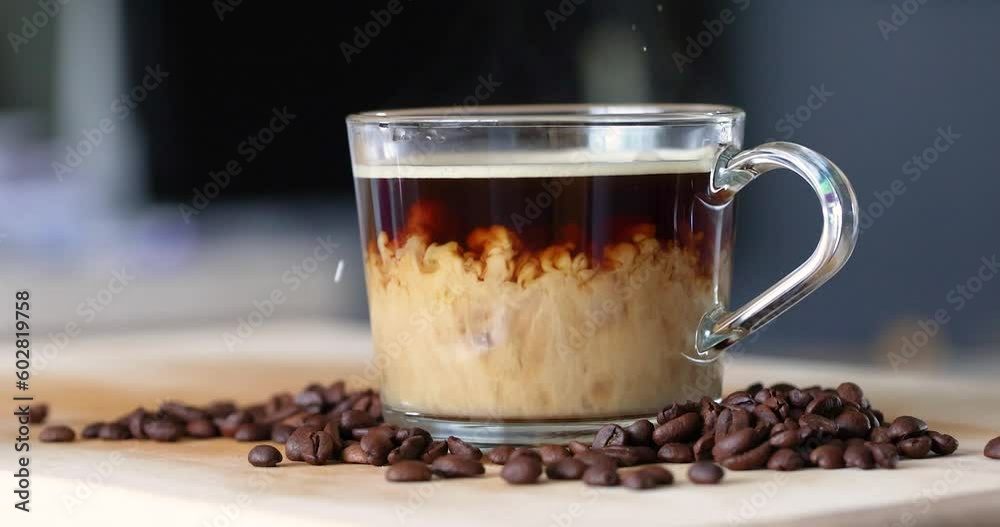 Cream added to hot coffee in a glass mug. Slow motion. Cream added to hot coffee in a glass mug. Slow motion.