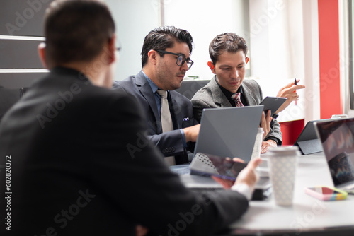 Group of young hispanic businessmen having meeting in conference room. Creative discussion business team using electronic devices, laptop, tablet, phone