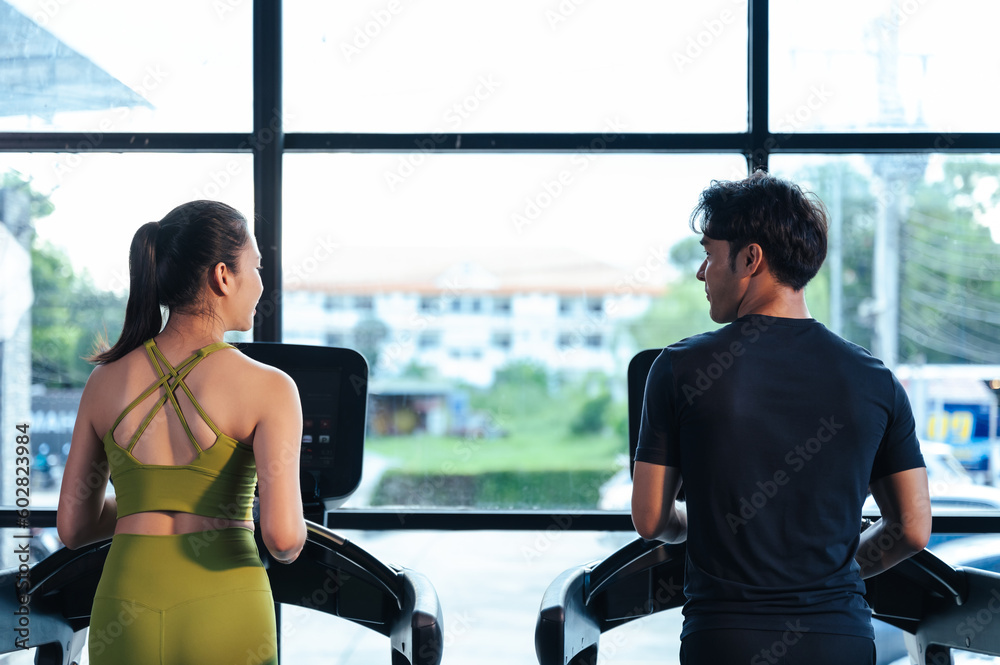 Obraz premium Behind together Asian man and woman healthy in sportswear cardio exercise jogging on a treadmill in fitness gym. Sport people workout indoor for good health. Healthy lifestyle concept.