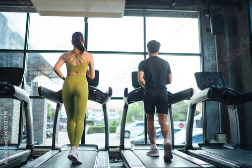 Behind together Asian man and woman healthy in sportswear cardio exercise jogging on a treadmill in fitness gym. Sport people workout indoor for good health. Healthy lifestyle concept.