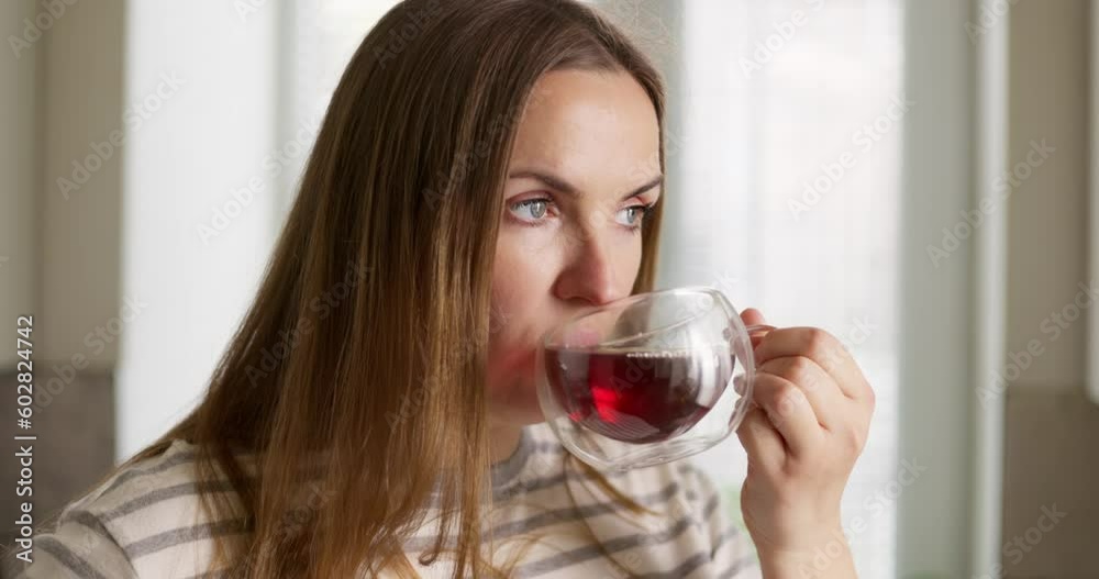 A woman drinks her hot tea, enjoying the taste and aroma in the kitchen A woman drinks her hot tea, enjoying the taste and aroma in the kitchen