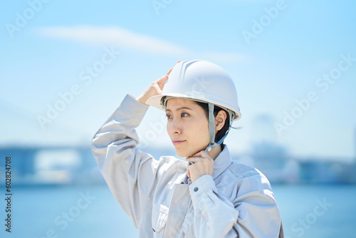 作業着を着てヘルメットを確認する女性 © maru54