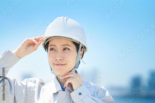 作業着を着てヘルメットを確認する女性 © maru54