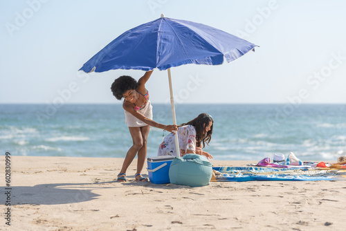 Friends laughing and opening the umbrella, on the shore of the beach © Guillermo Spelucin