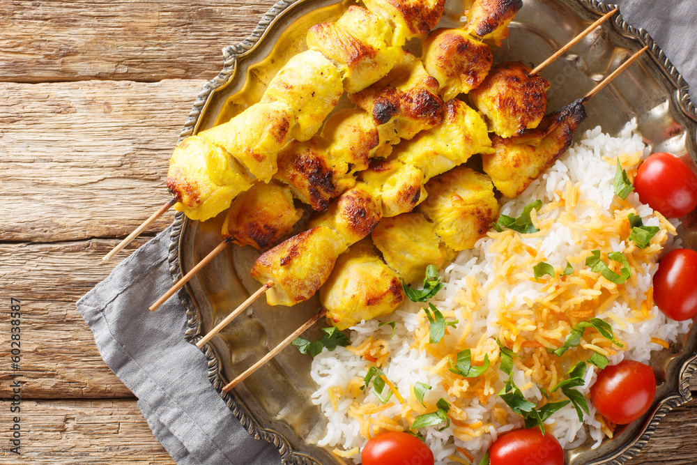Grilled saffron chicken skewers with rice garnish close-up in a plate on a wooden table. horizontal top view from above
