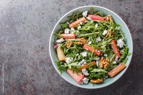 Diet salad with baked rhubarb, arugula, goat cheese and walnuts close-up in a bowl on the table. Horizontal top view from above