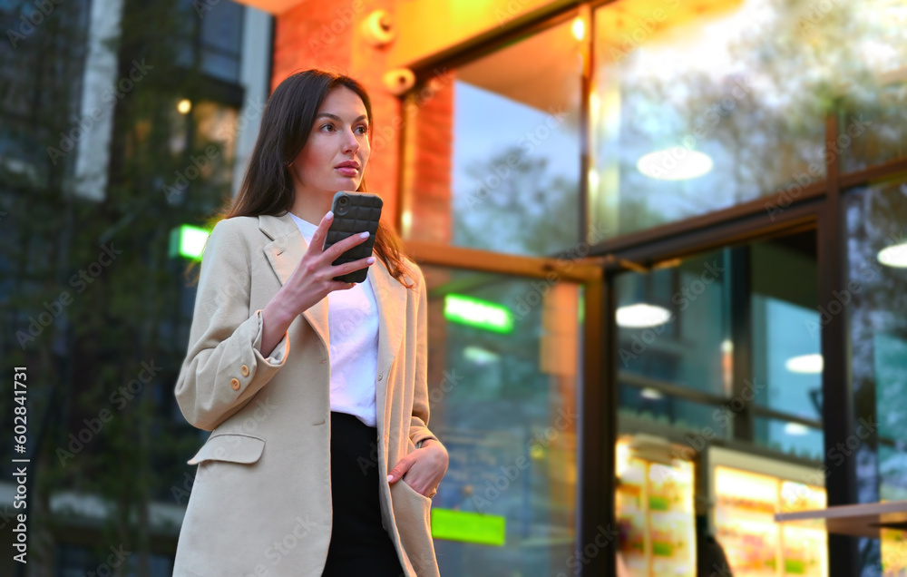 A beautiful woman dressed in casual attire is enjoying a cup of coffee in an urban setting. She appears to be deep in conversation as she speaks on her phone, with an expression