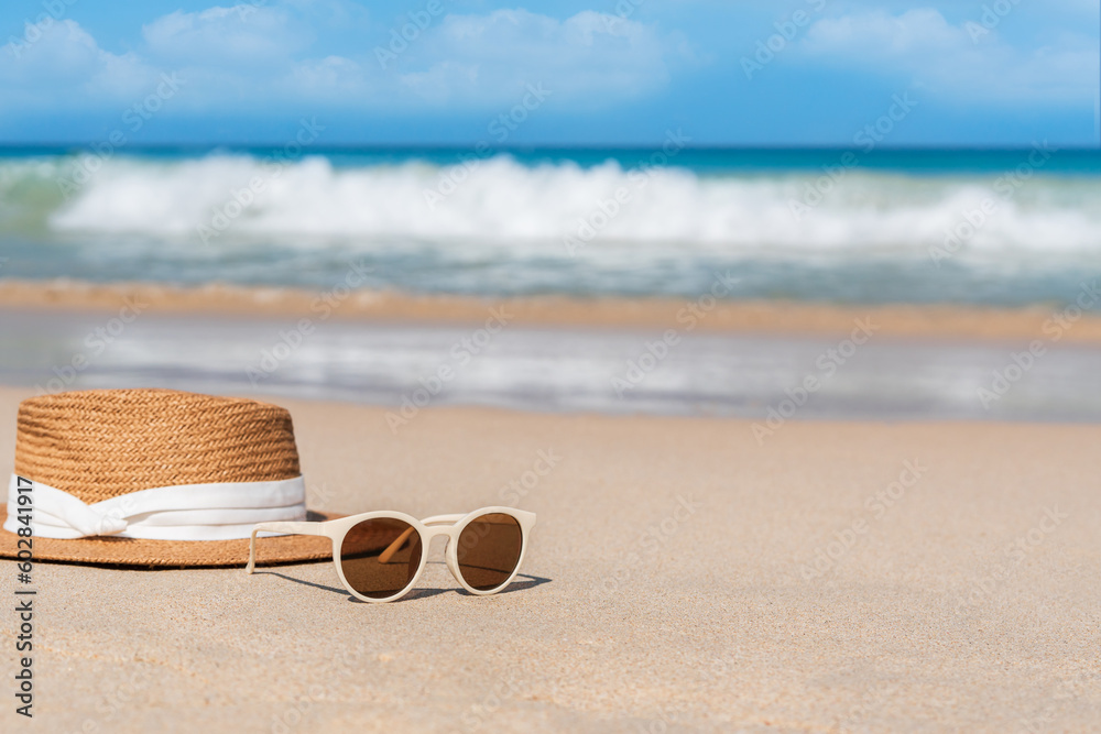 Sunglasses and straw hat on sandy beach at tropical seaside on warm sunny day. Summer vacation concept.  Copy space