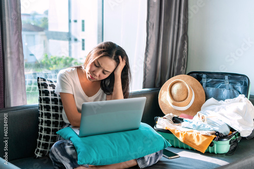 Stressed Asian woman worried about online booking errors or making the wrong travel plans on her summer vacation. Sadness girl fell down due to the trip has been cancelled. Travel and holiday concept.