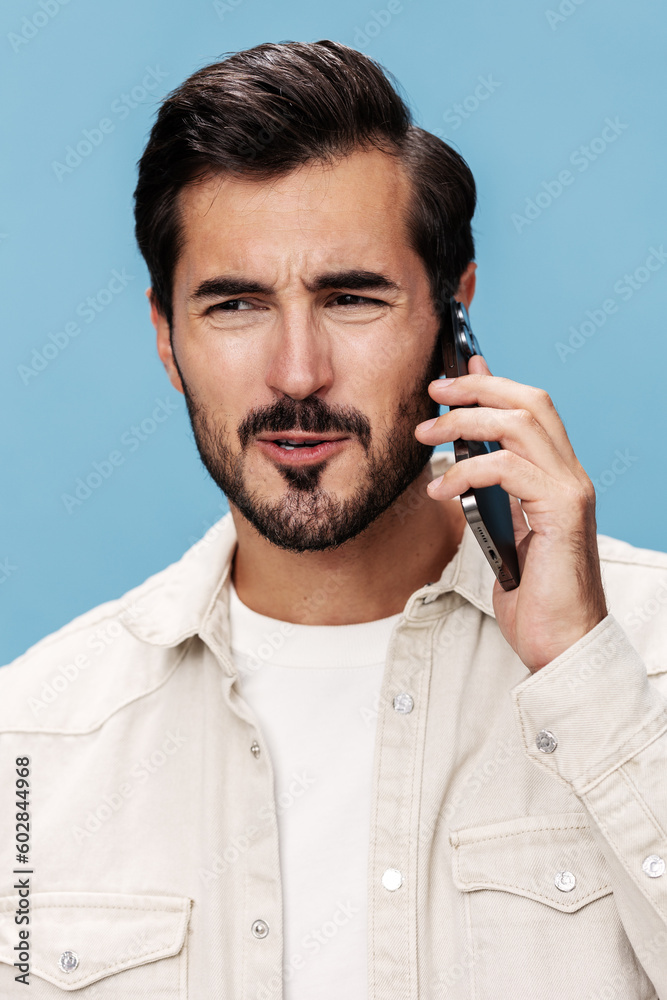 Portrait of male brunette anger talking on the phone in close-up, disgruntled, on a blue background in a white T-shirt and jeans, copy space Portrait of male brunette anger talking on the phone in close-up, disgruntled, on a blue background in a white T-shirt and jeans, copy space