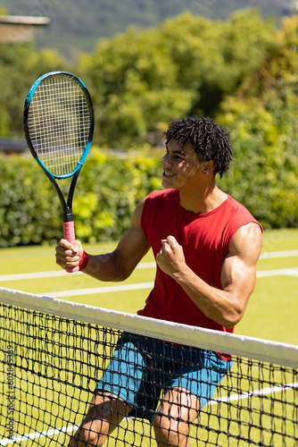 Happy biracial man with racket celebrating win on sunny outdoor tennis court © wavebreak3
