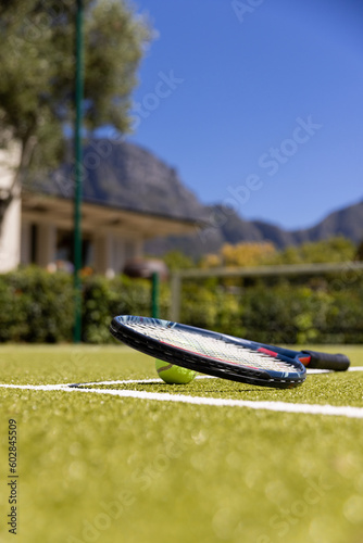 Tennis ball and tennis racket lying on sunny outdoor grass tennis court, with copy space