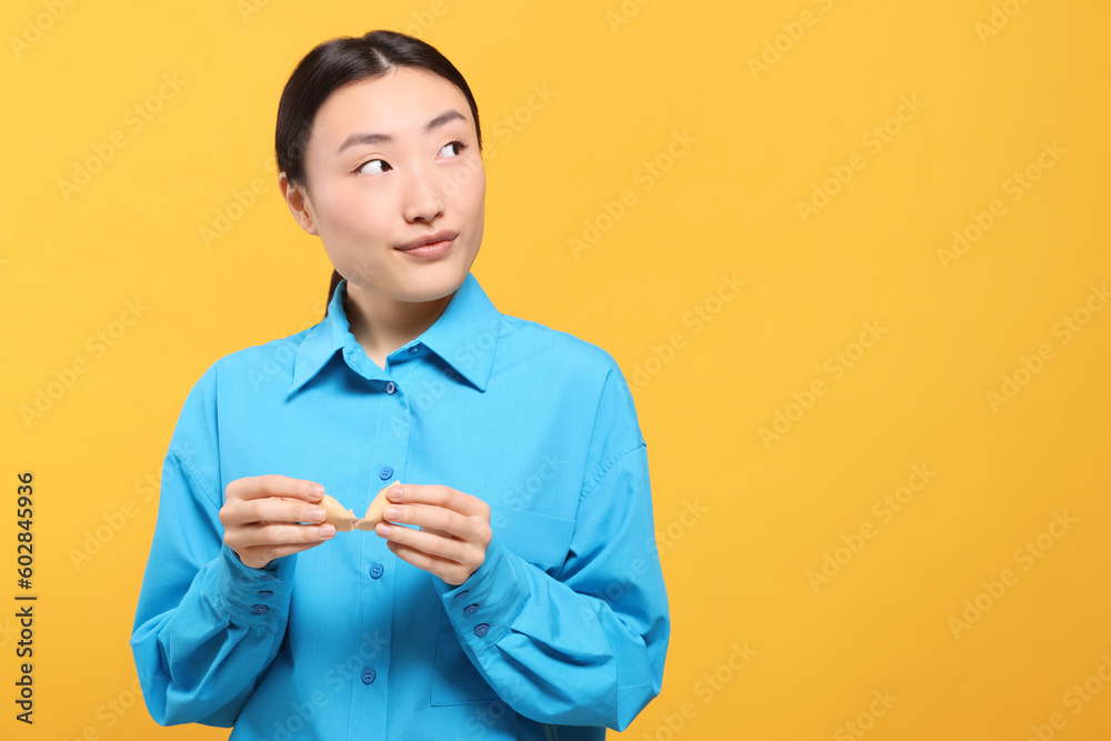Asian woman breaking tasty fortune cookie with prediction on yellow background, space for text Asian woman breaking tasty fortune cookie with prediction on yellow background, space for text