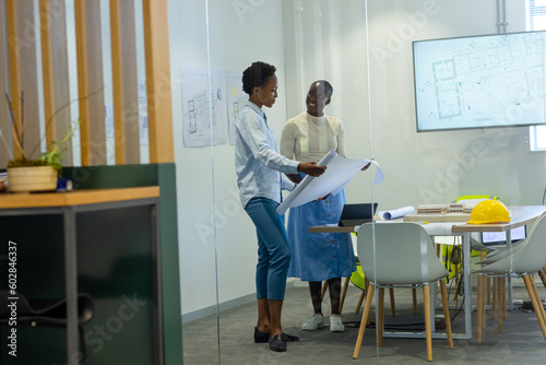 African american female professionals discussing blueprint in office seen through glass wall