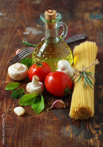 Spaghetti, tomatoes, olive oil, mushrooms and herbs on an old wooden table. Italian cuisine. Dark background. 