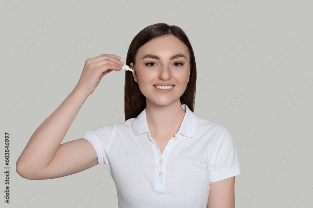 Young woman using ear drops on light grey background Young woman using ear drops on light grey background