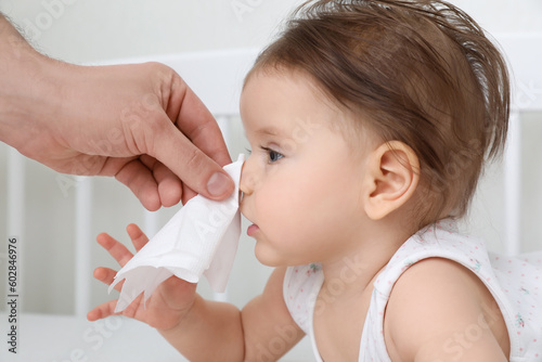 Father wiping runny nose of little baby with napkin on bed, closeup