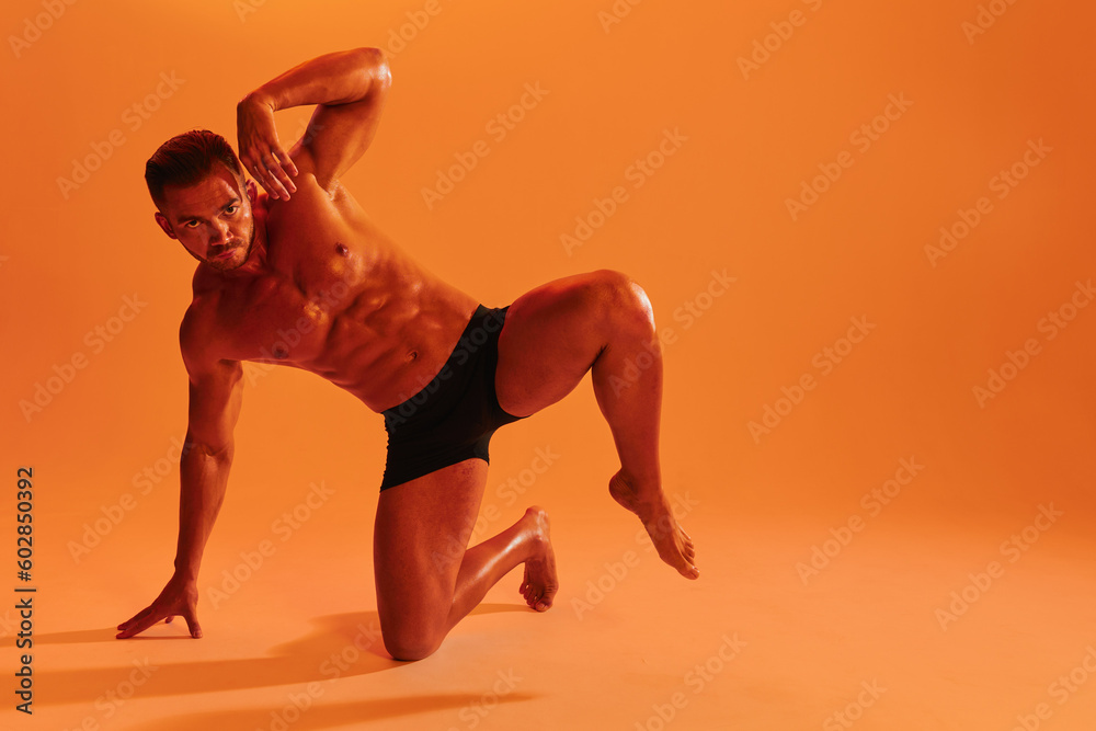 Man athletic bodybuilder poses with nude torso abs full-length in the background. Advertising, sports, active lifestyle, color light, competition, challenge concept. 