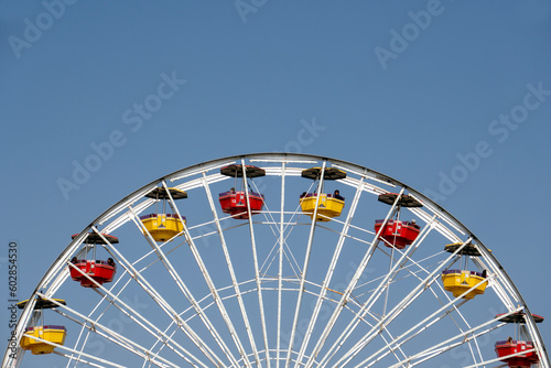 A view of a the top half of a Ferris Wheel with colorful cabins on a sunny day